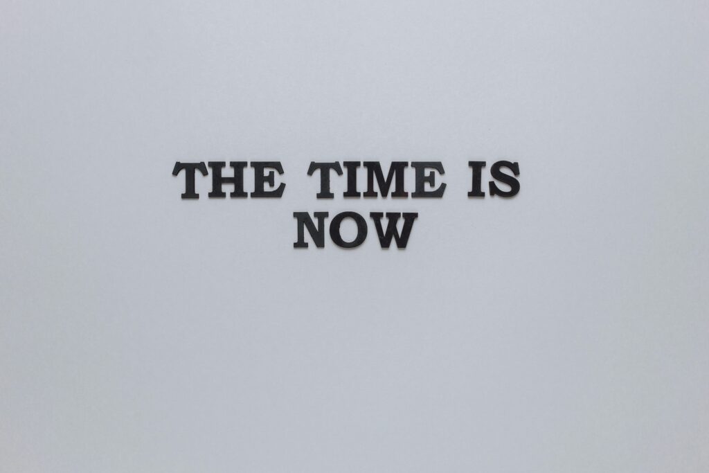 Minimalist poster with the motivational quote 'The Time is Now' on a gray background.